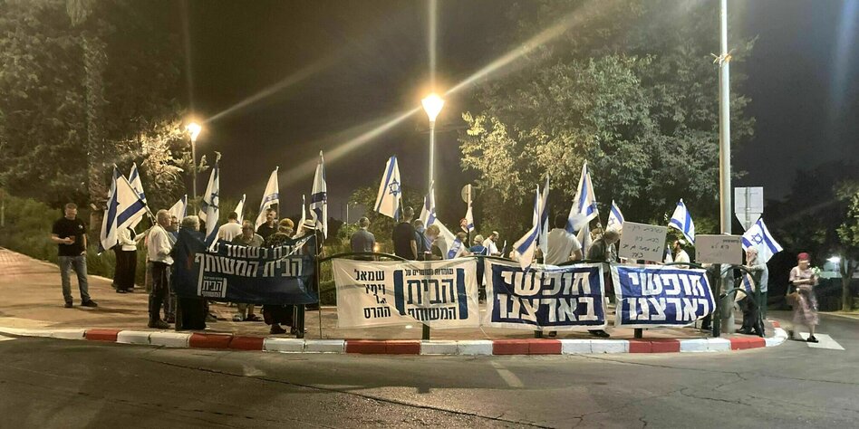 Orthodoxe Siedler stehen abends mit israelischen Fahnen und Transparenten auf einem Bürgersteig