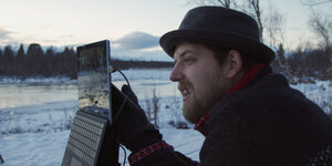 Jonathan „Jonny“ Schüddekopf mit einem aufgeklappten Laptop vor einer verschneiten Winterlandschaft