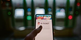 Eine Hand hält ein hell leuchtendes Smartphone, darauf steht "D-Ticket"