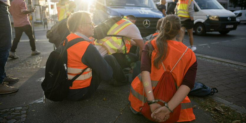 Menschen in Warnwesten sitzen auf einer Straße.