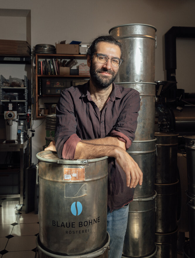 Ein Mann steht neben großen Weißblechtonner voller frisch geröstetem Kaffee: Pablo Fuchs, Inhaber der "Blauen Bohne"