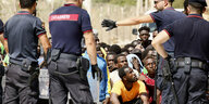 Menschen aus Afrika sitzen am Boden vor italienischen Polizisten