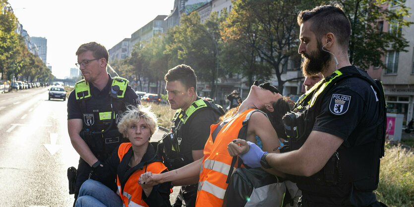 Drei Polizisten führen zwei Aktivist:innen der Klima-Gruppe Letzte Generation ab.