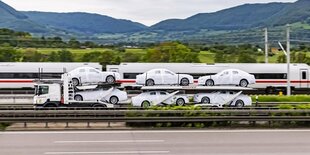 Ein Autotransporter auf der Autobahn vor einem ICE.