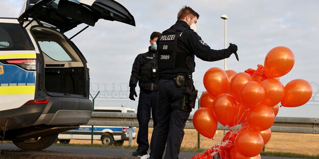 Ein Polizeibeamter zersticht orange-farbene Luftballons mit einem Messer
