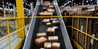 Das Foto zeigt Pakete auf dem offenbar schnell laufenden Fließband des Versandhandels Amazon.