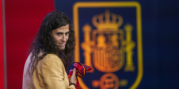 Spanienes neue Nationaltrainerin Montse Tomé mit einem verschmitzten Grinsen vor dem Wappen des spanischen Fußballverbands