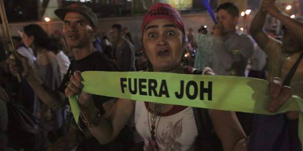 Eine Demonstrantin mit Banner in der Hand guckt in die Kamera