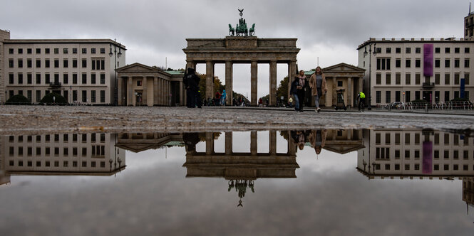 Der Pariser Platz am Brandenburger Tor bei Regenwetter - das Tor spiegelt sich in der Regenpfütze