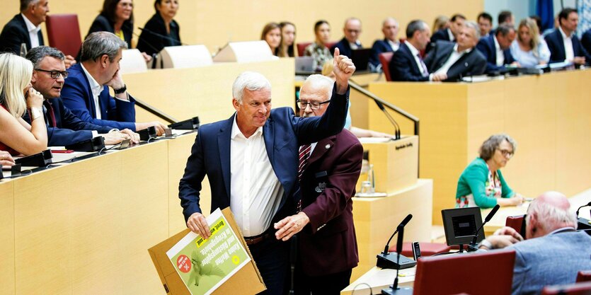 Rolf Stadler reckt die Hand, er wird von einem Saaldiener gbedrängt, der ihm das Plakat in seiner Hand wegnehmen muss