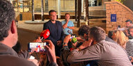 Vicor Franco im Anzug hinter Pressemikrofonen. Journalisten stehen vor ihm.