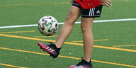 Ein Mädchen auf einem Fußballplatz kickt einen Ball in die Luft.