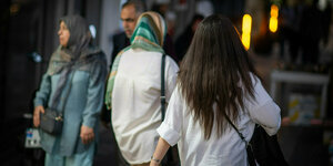Eine Frau läuft mit offenen Haaren am Abend eine Straße entlang, im Hintergrund laufen zwei Frauen mit Kopftuch.