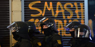 Ein Polizeiaufgebot steht am 18.03.2015 in Frankfurt (Hessen) am Rande der Demonstrationen gegen die offiziellen Eröffnung der Europäischen Zentralbank (EZB) in der Innenstadt vor einem Graffiti.