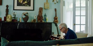 Ein Mann sitzt mit einer Gitarre auf einem Sofa