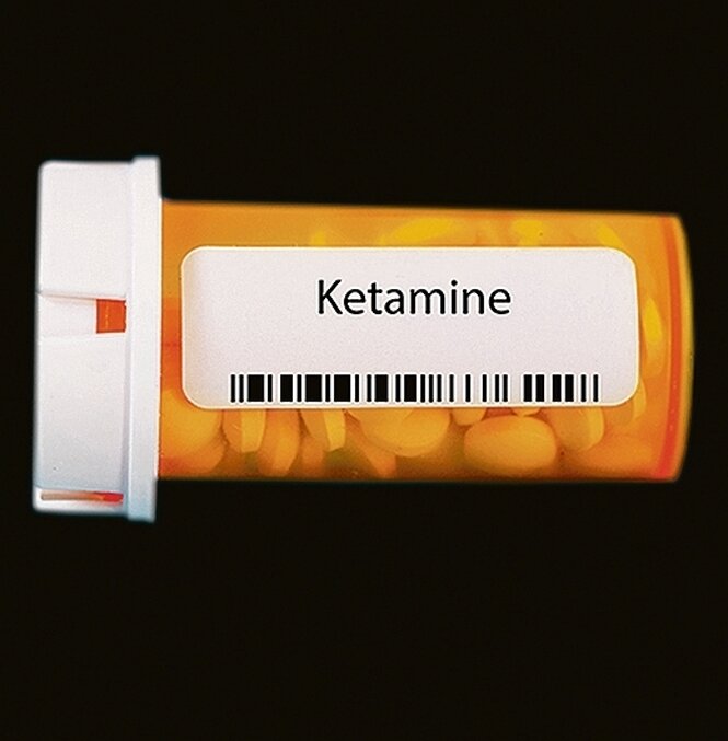 Eine Pillendose mit der Aufschrift "Ketamine" vor schwarzem Hintergrund