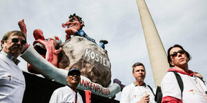 Protestierende Menschen vor einem Karnevalswagen, auf dem Karl Lauterbach abgebildet ist