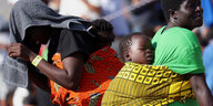 Eine Frau in einer Menschenmenge trägt ein Kleinkind auf ihrem Rücken