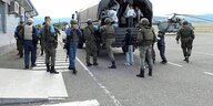 Soldaten mit Blauhelmabzeichen stehen an einem Lastwagen, auf den Bewohner Berg Karabachs klettern, im Hintergrund steht ein Hubschrauber