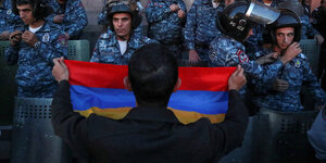 Ein Mann hält mehreren Soldaten die Armenische Flagge vor
