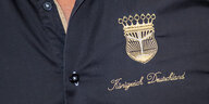 Der Schriftzug "Königreich Deutschland" und ein Wappen sind auf einem schwarzen Hemd von Peter Fitzek zu sehen.