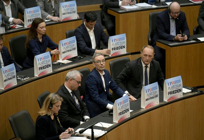 FPÖ-Abgeordnete im Parlament. Vor ihnen sind Schilder auf denen Steht "Paltz für Friden - Platz für Neutralität"