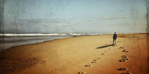 Ein Mann geht den Strand entlang, man sieht seine Fußspuren im Sand