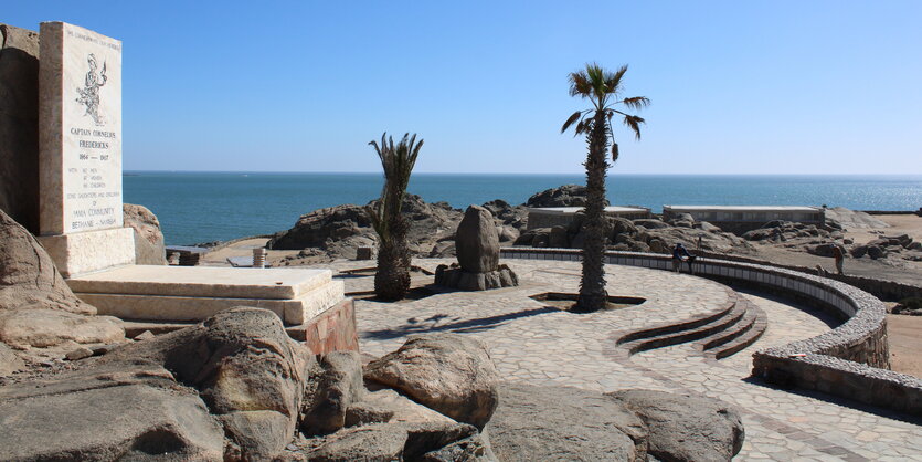 Zeigt einen Gedenkstein und den Platz davor auf der kargen, felsigen Insel vor der namibischen Stadt Lüderitz, wo sich früher das Nama-Lager befand.