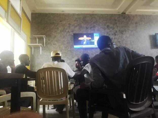 Eine Gruppe von Männern sitzt auf weissen Plastikstühlen in einem Kaffee, der Fernseher an der Wand bringt Nachrichten Eine Gruppe von Männern sitzt auf weissen Plastikstühlen in einem Kaffee, der Fernseher an der Wand bringt Nachrichten