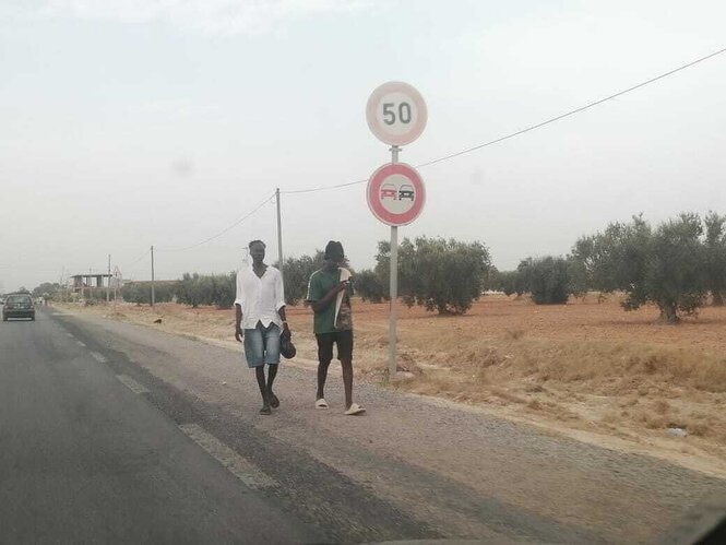 Zwei junge schwarze Männer gehen an einer staubigen Straße entlang, die wenig befahren ist