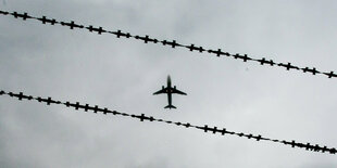 Flugzeug im Himmel vor Stacheldrahtzaun