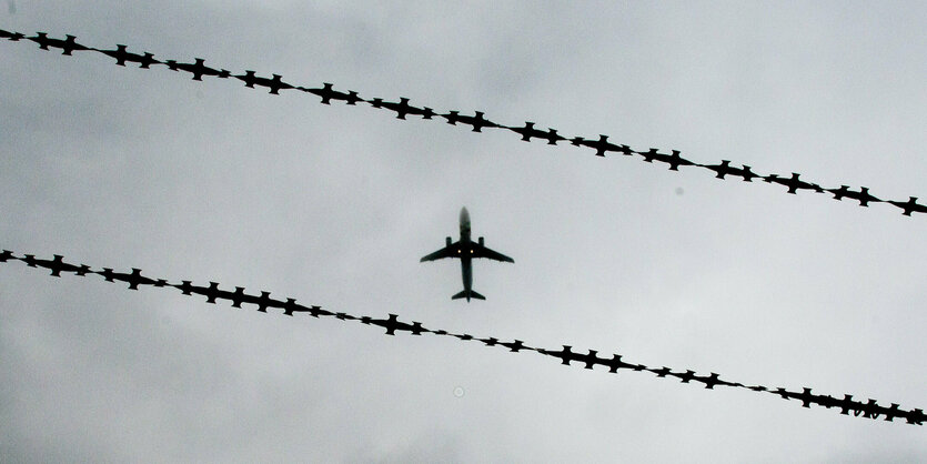 Flugzeug im Himmel vor Stacheldrahtzaun