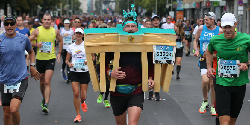 Ein Läufer beim Berlin-Marathon mit einem Brandenburger Tor aus Pappmaché