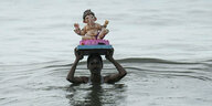 Eine Person ragt aus dem Wasser und trägt eine Statue auf dem Kopf.