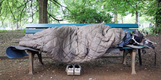 Obdachloser liegt mit einem Schlafsack zugedeckt auf einer Bank