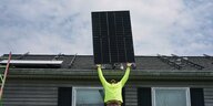 Mann hebt Teil einer Solaranlage auf ein Hausdach