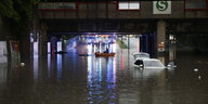 Einsatzkräfte der Feuerwehr fahren mit einem Schlauchboot zu den Autos in einer überschwemmten Unterführung.