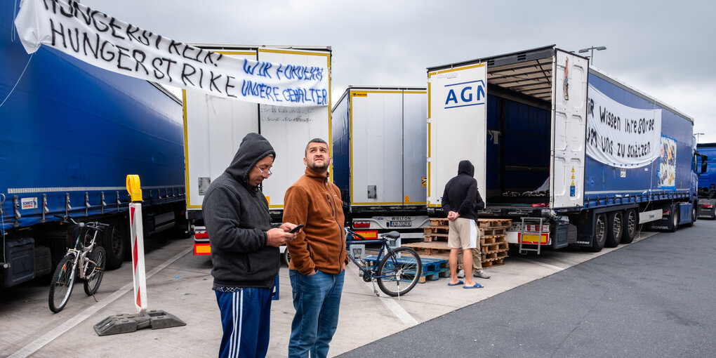 Zwei Männer stehen vor einem LKW und einen Banner. Auf dem Banner steht: Hungerstreik! Wir fordern unseren Lohn