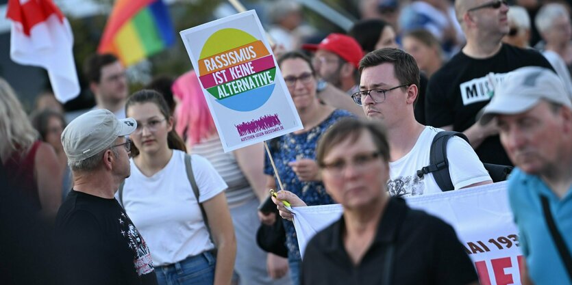 Protestierende Menge - ein Mann hält ein kleines Plakat hoch: Rassismus ist keine Alternative