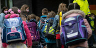 Erstklässler mit ihren Schultaschen warten bei der Einschulung auf den gemeinsamen Gang in ihr Klassenzimmer.