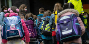 Erstklässler mit ihren Schultaschen warten bei der Einschulung auf den gemeinsamen Gang in ihr Klassenzimmer.