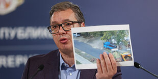 Aleksandar Vucic hält ein Foto hoch, das eine Barrikade von drei Lastwagen zeigt, die eine Brücke in der Nähe des Klosters versperren sollen