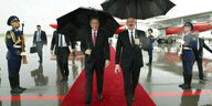 Zwei Männer laufen durch den Regen unter schwarzen Schirmen