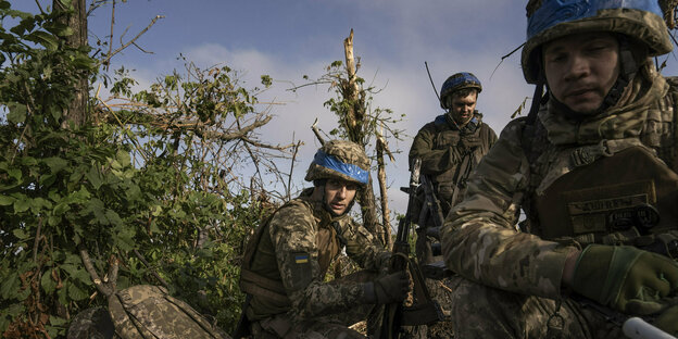 Drei Ukrainische Soldaten an der Front im Gebiet Donezk, September 2023, kauern bewaffnet und in Uniform in einem Gestrüpp