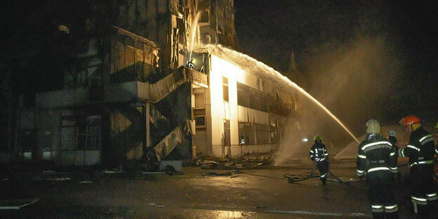 Feuerwehrleute ziehlen mit einem Wasserstrahl auf ein zerstörtes Gebäude in der Nacht.