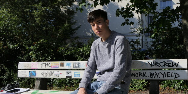 Der junge Geflüchtete Nagiballah Hashimi sitzt auf einer Bank und schaut ernst in die Kamera.