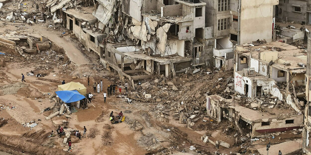 Blick auf zerstörte Häuser, Luftbild auf dem zu sehen ist, wie Menschen Zelte vor den eingestürzten Häusern aufstellen