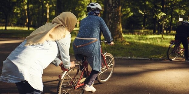 Eine Frau mit Kopftuch hält ein Fahrrad mit einer anderen Frau fest