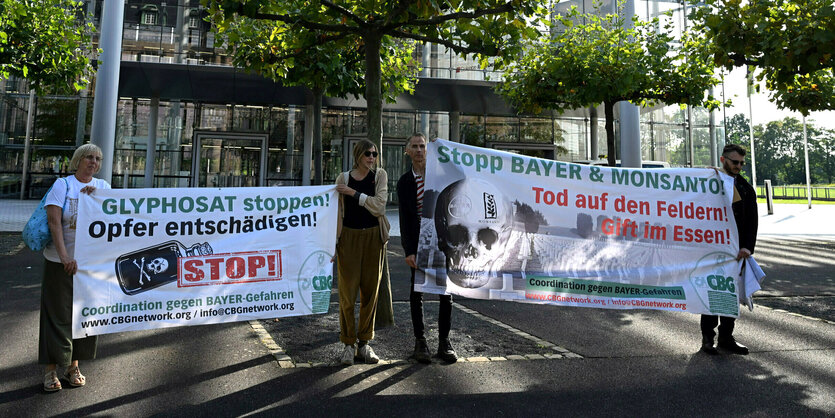 Vier Personen halten vor der Konzernzentrale von Bayer-Konzernzentrale Banner in den Händen; Glyphosat stoppen ! Opfer entschädigen ! Stop !