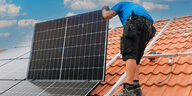 Ein Mann installiert auf einem Dach eine Photovoltaikanlage
